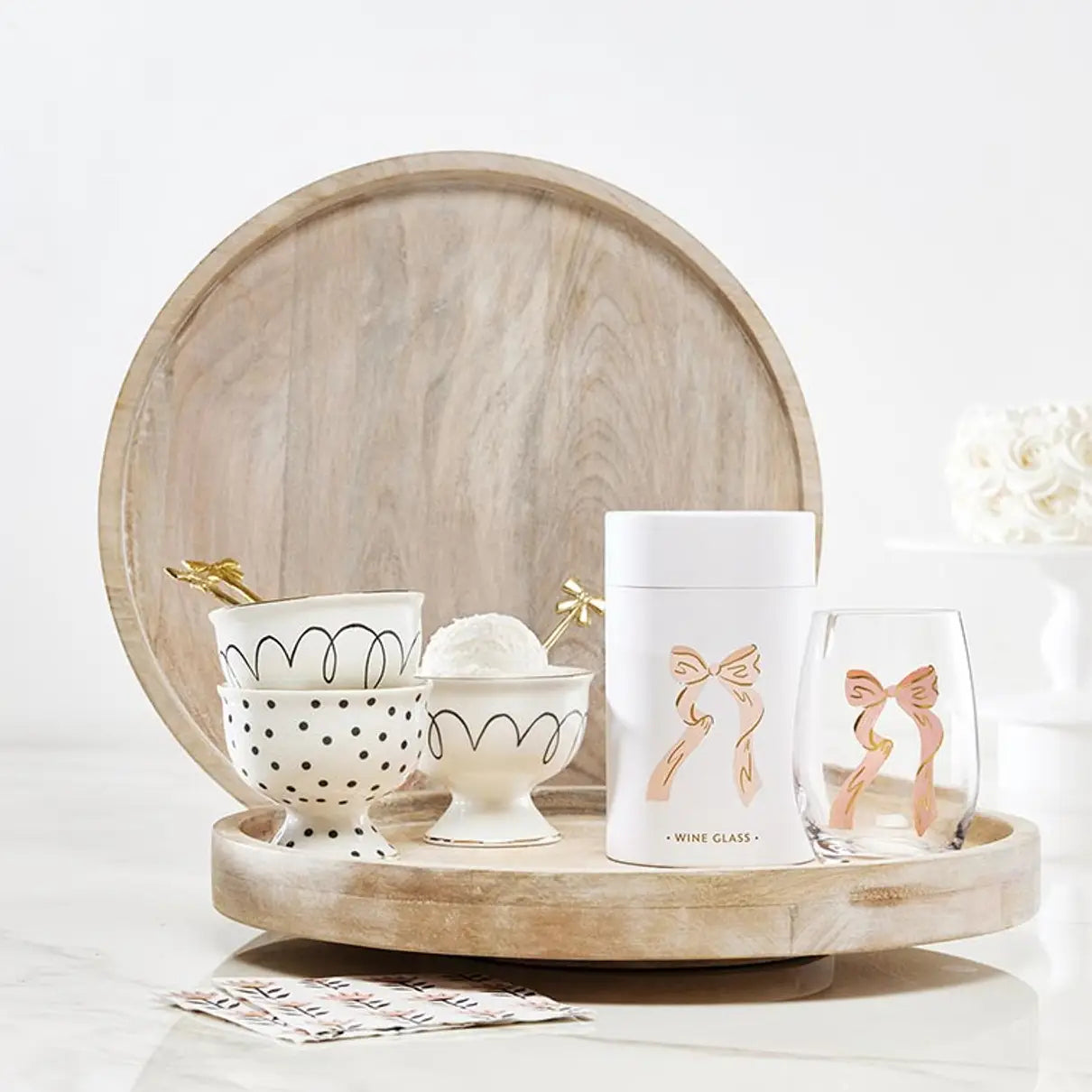 Set of decorative bowls and glasses with bow designs on a wooden tray.