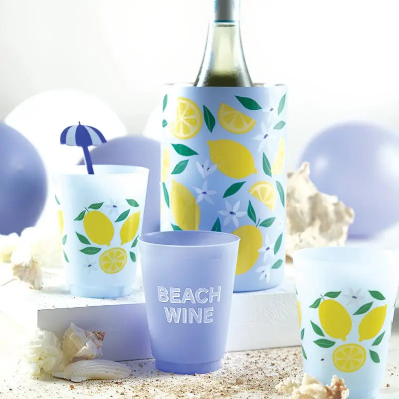 Wine bottle with lemon design, glasses, and beach-themed decor on a sandy background