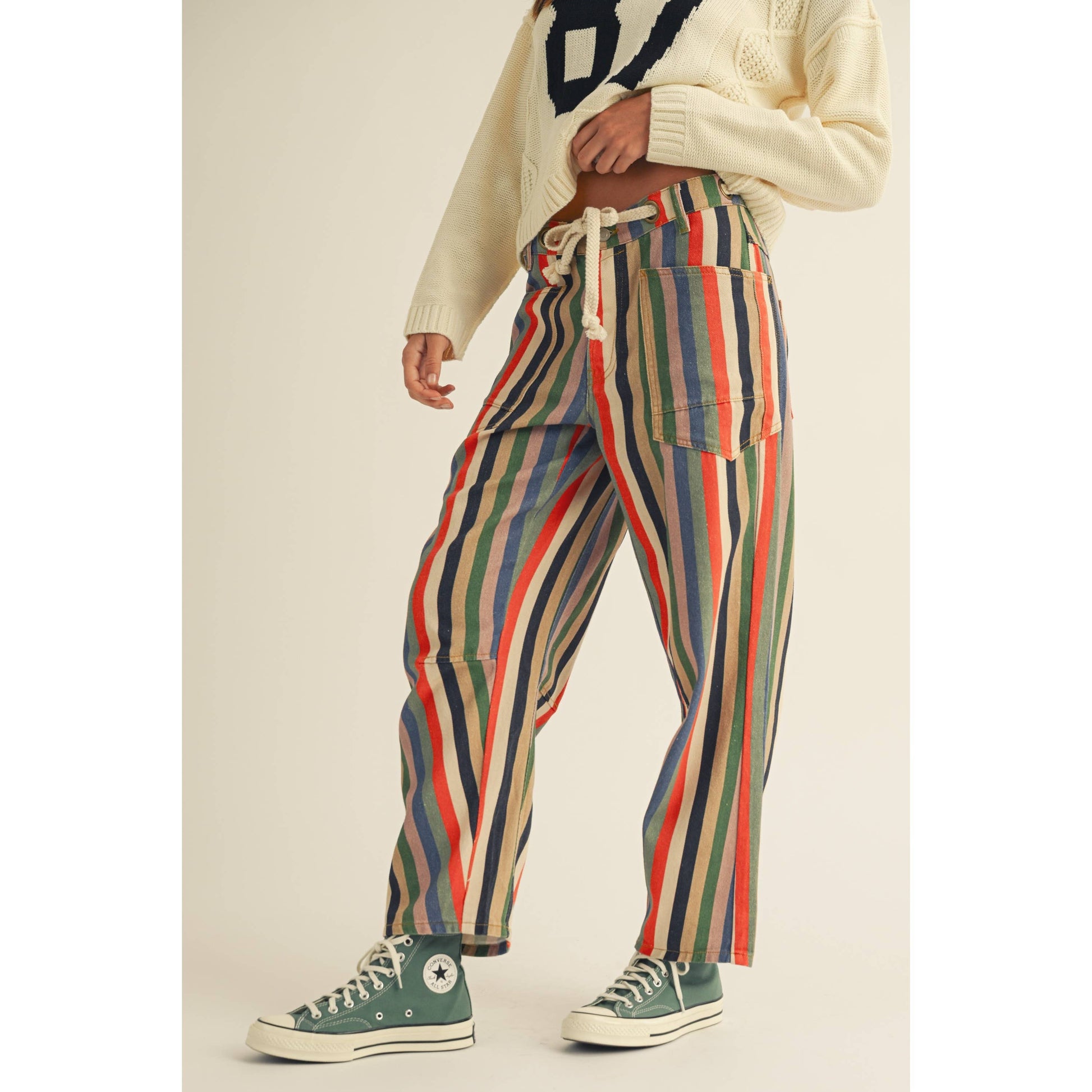 Person wearing colorful striped pants and green Converse shoes on a plain background