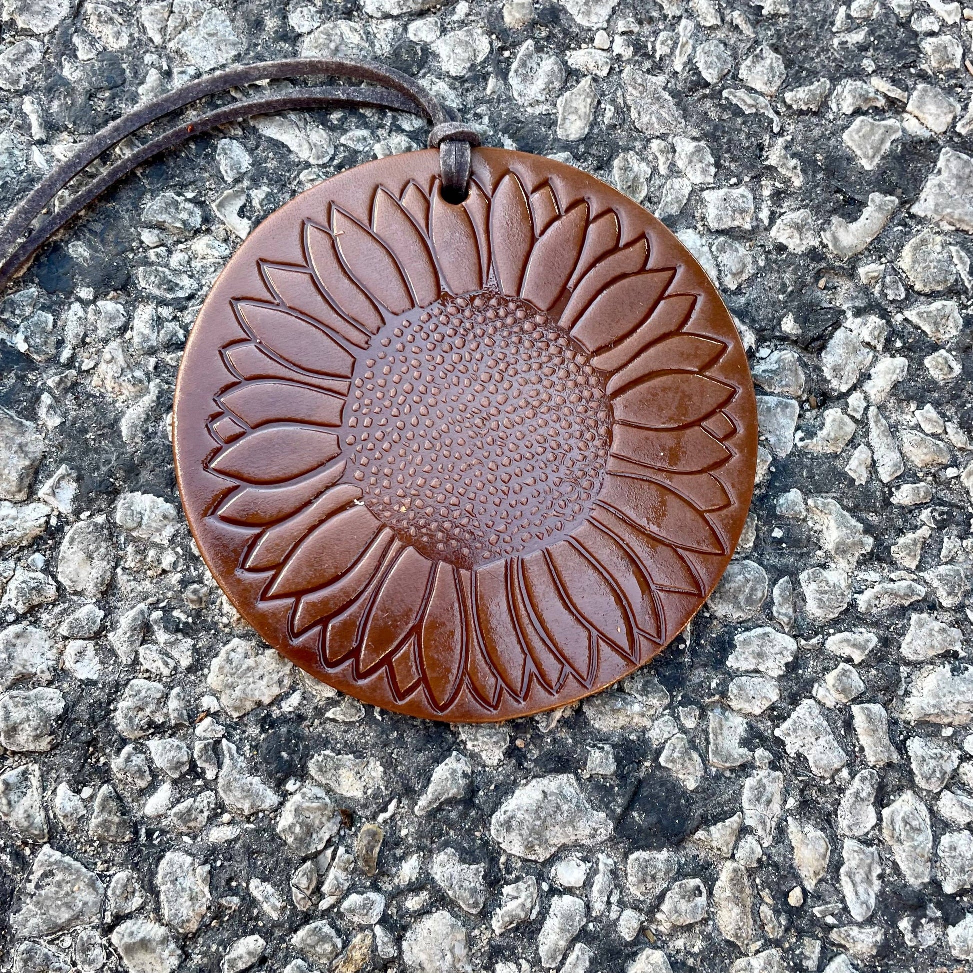 Brown leather sunflower pendant on a textured surface