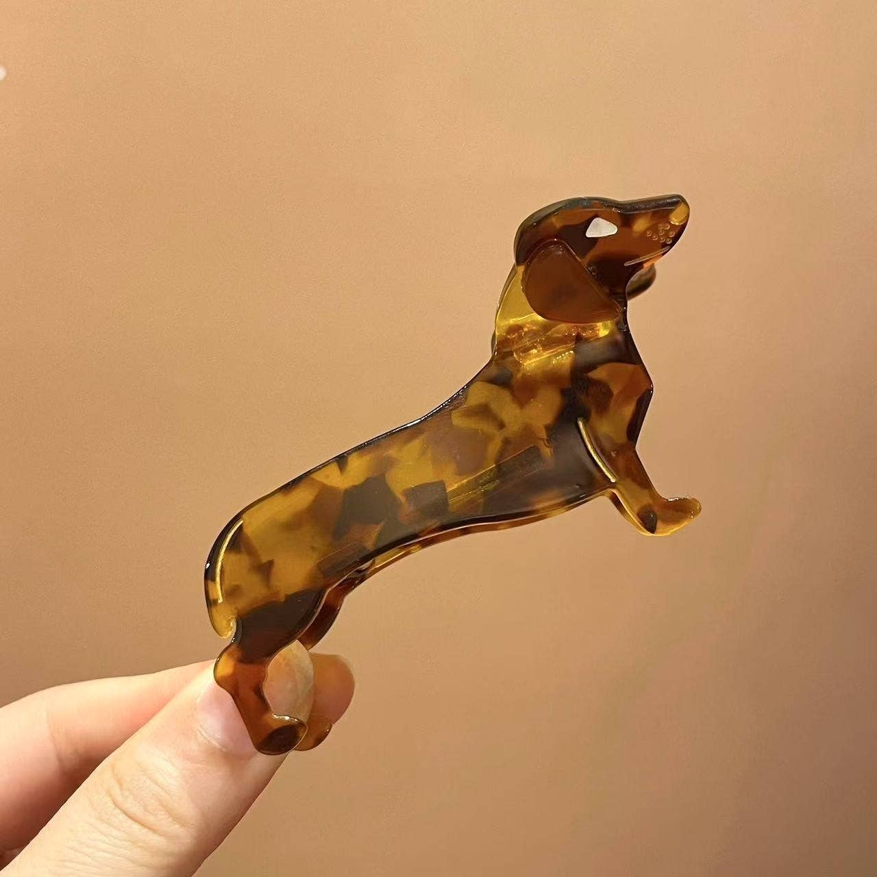 Tortoiseshell dog-shaped hair clip held against a beige background