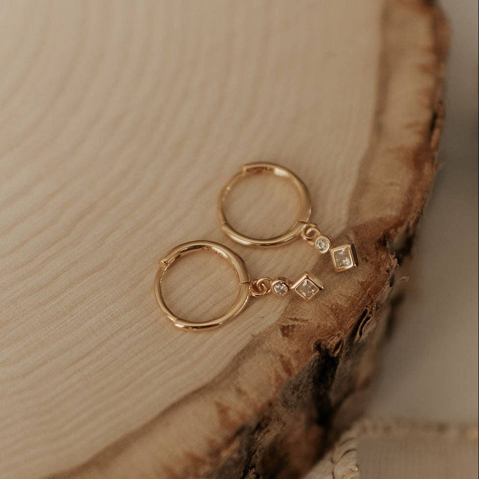 Gold hoop earrings with small diamond-like stones on a wooden surface