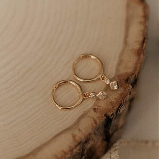 Gold hoop earrings with small diamond-like stones on a wooden surface