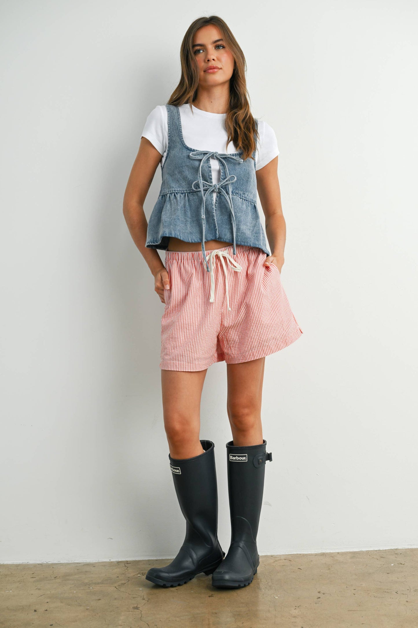 Woman wearing a denim top with pink shorts and black rain boots 