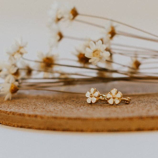 Gold flower-shaped earrings on a wooden surface with a blurred floral background