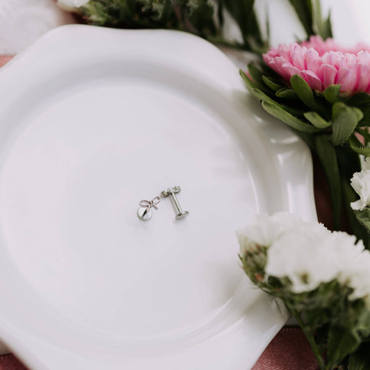 Silver earring on a white plate with flowers in the background