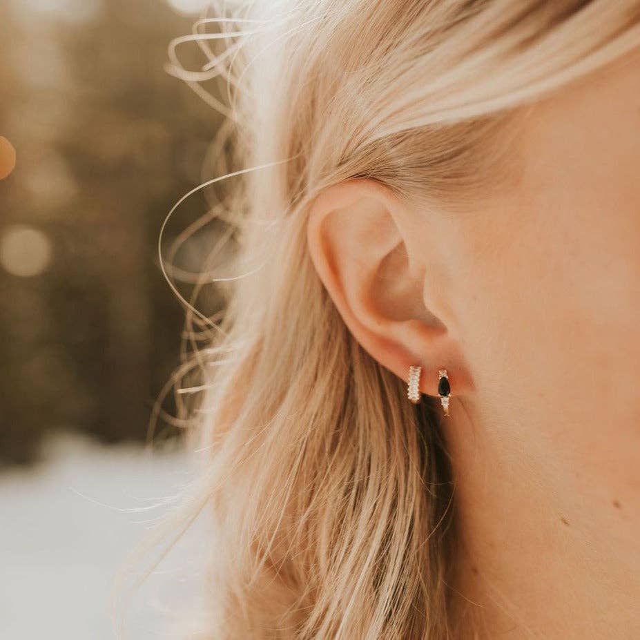 Close-up of a person wearing two earrings with a blurred natural background