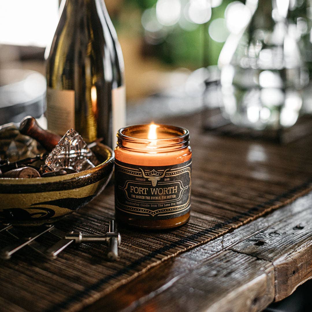 Candle with 'Fort Worth' label on a wooden surface with blurred background
