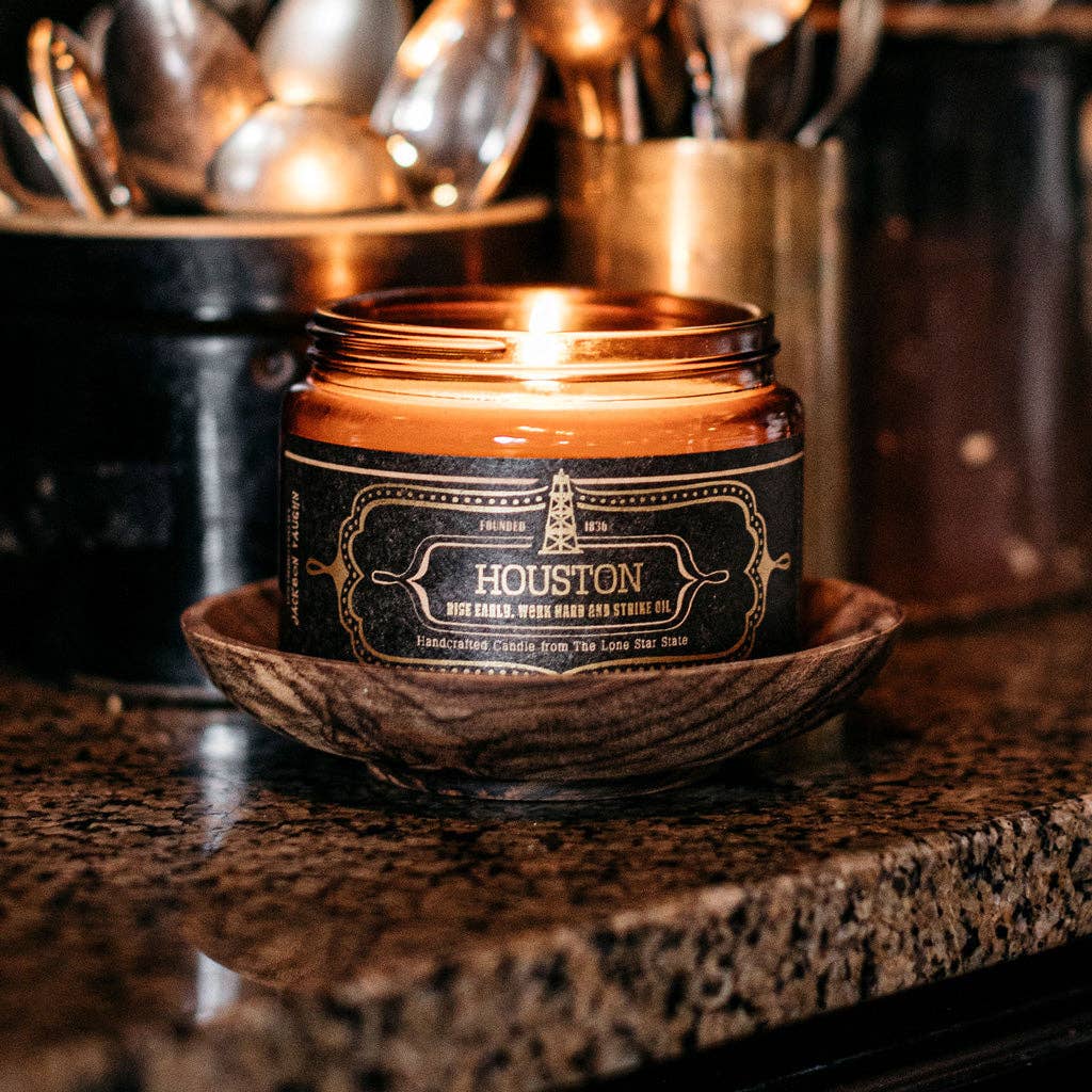 Candle in a decorative container with 'Houston' branding on a dark surface.
