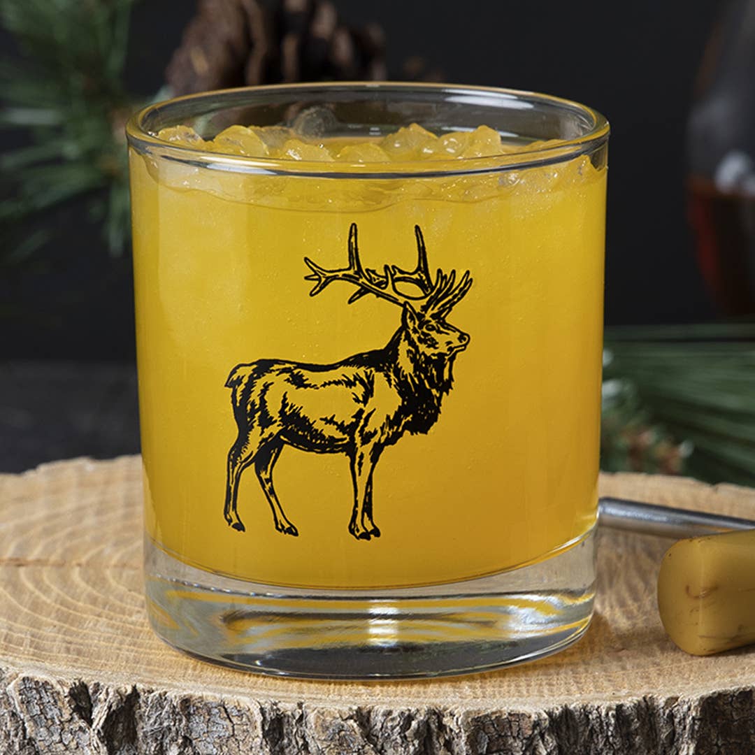 Glass with yellow liquid and deer illustration on a wooden surface