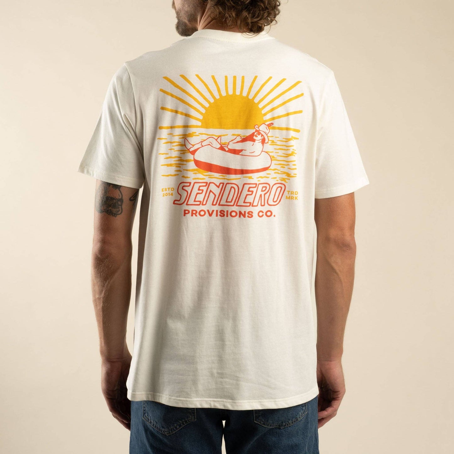 Person wearing a white t-shirt with a graphic design and text on the back, on a beige background