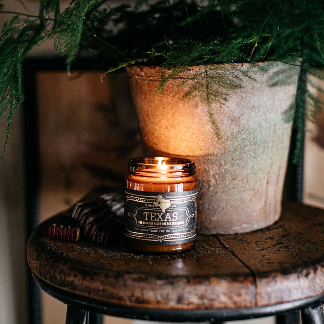 Candle labeled 'Texas' on a wooden surface with a blurred background