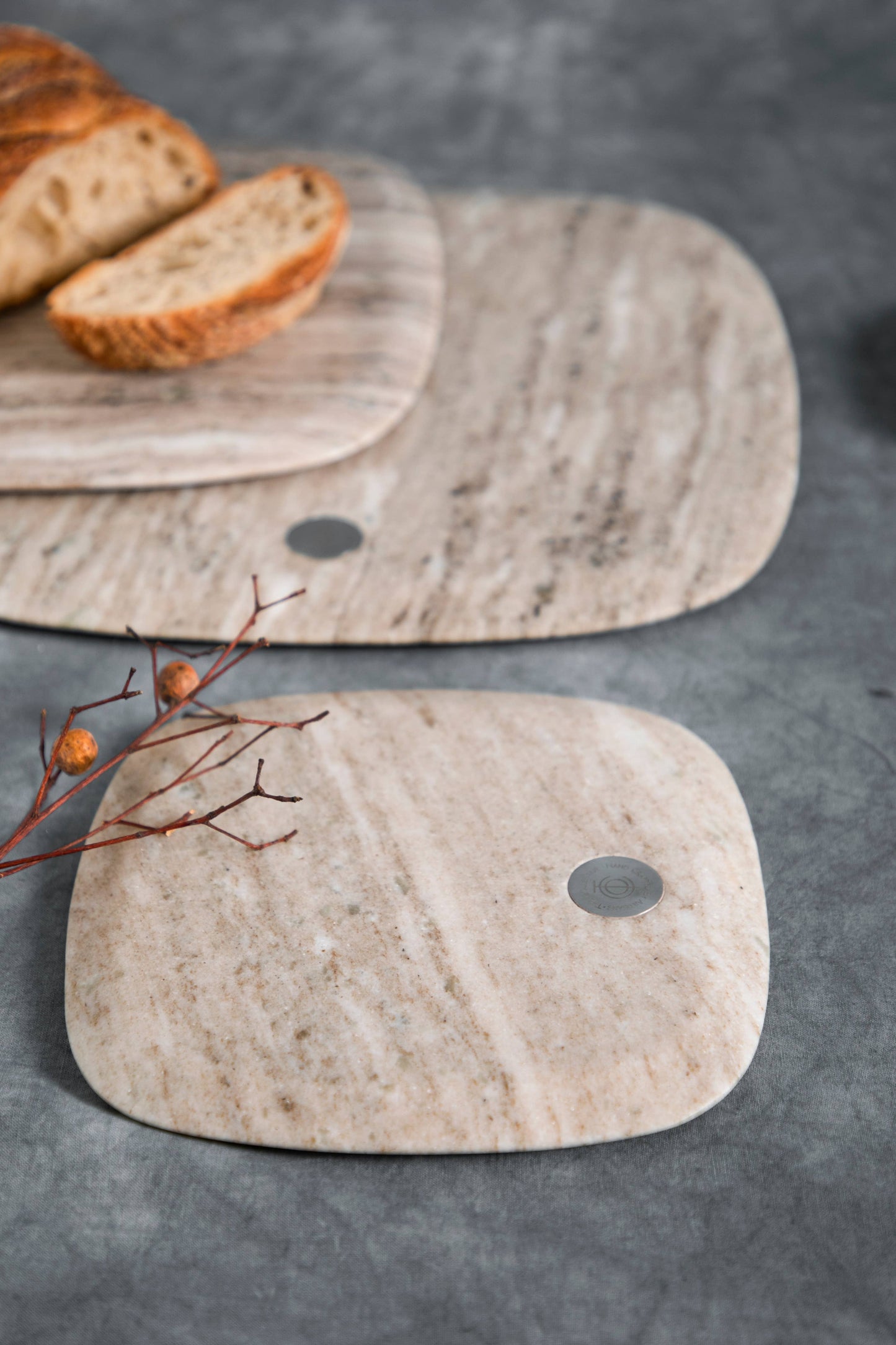 Two stone cutting boards on a gray surface with bread slices and a branch.