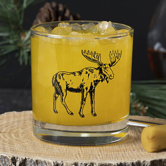 Glass with yellow liquid and moose illustration on a wooden surface