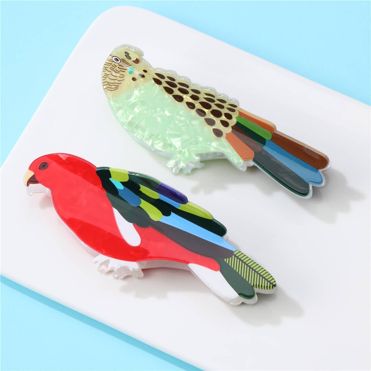 Two colorful bird-shaped clips on a white surface with a light blue background