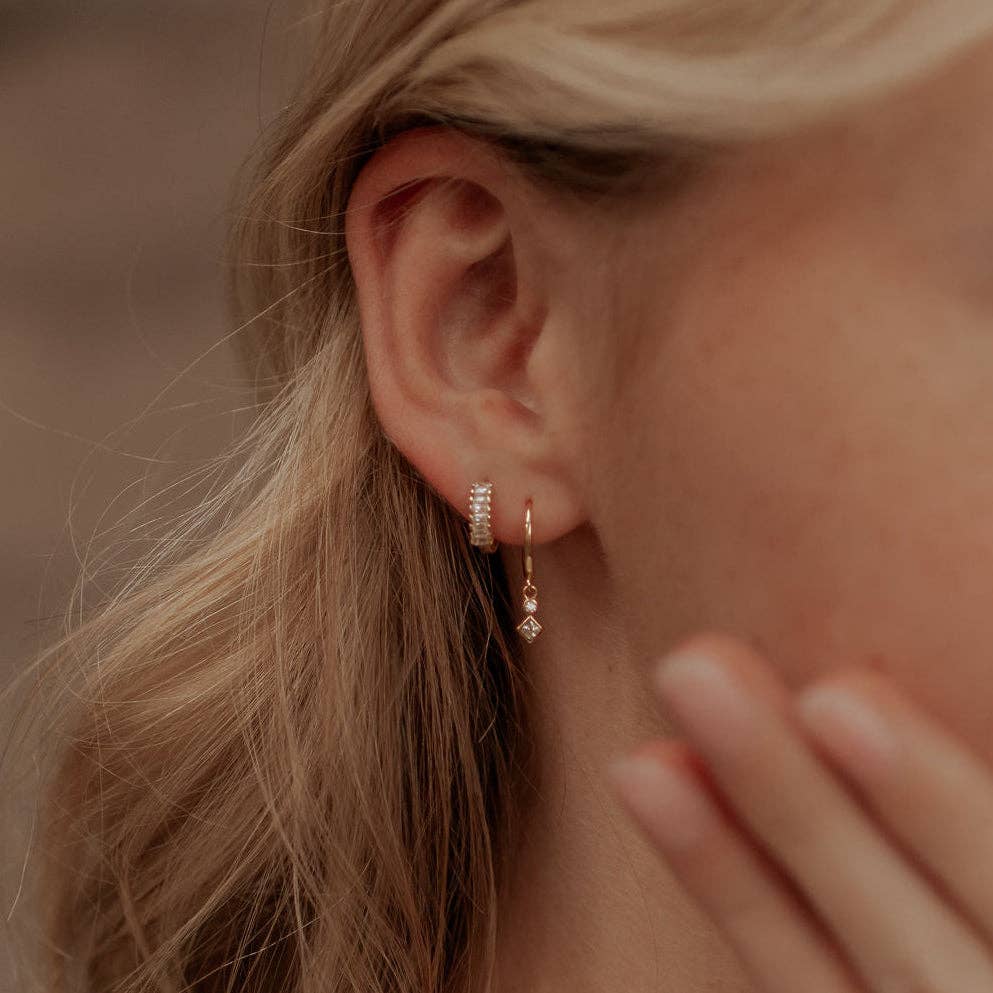 Close-up of a person wearing gold hoop earrings with a blurred background