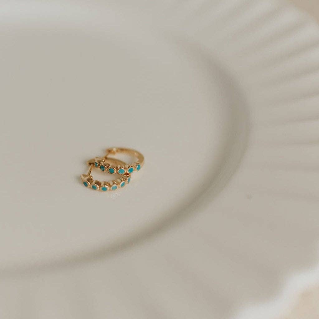 Gold earrings with turquoise stones on a beige plate