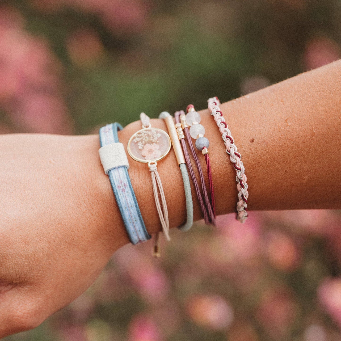 Close-up of a wrist wearing multiple colorful bracelets with a blurred floral background
