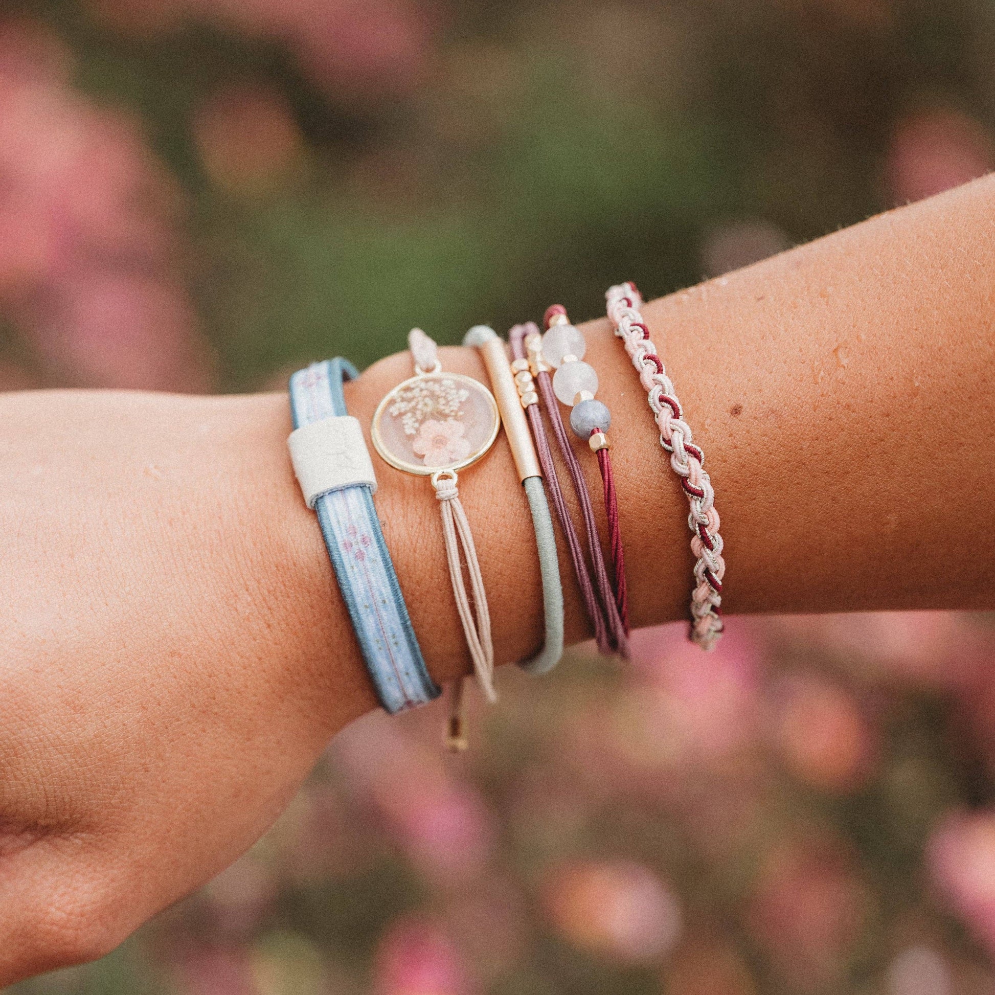 Close-up of a wrist wearing multiple colorful bracelets with a blurred floral background