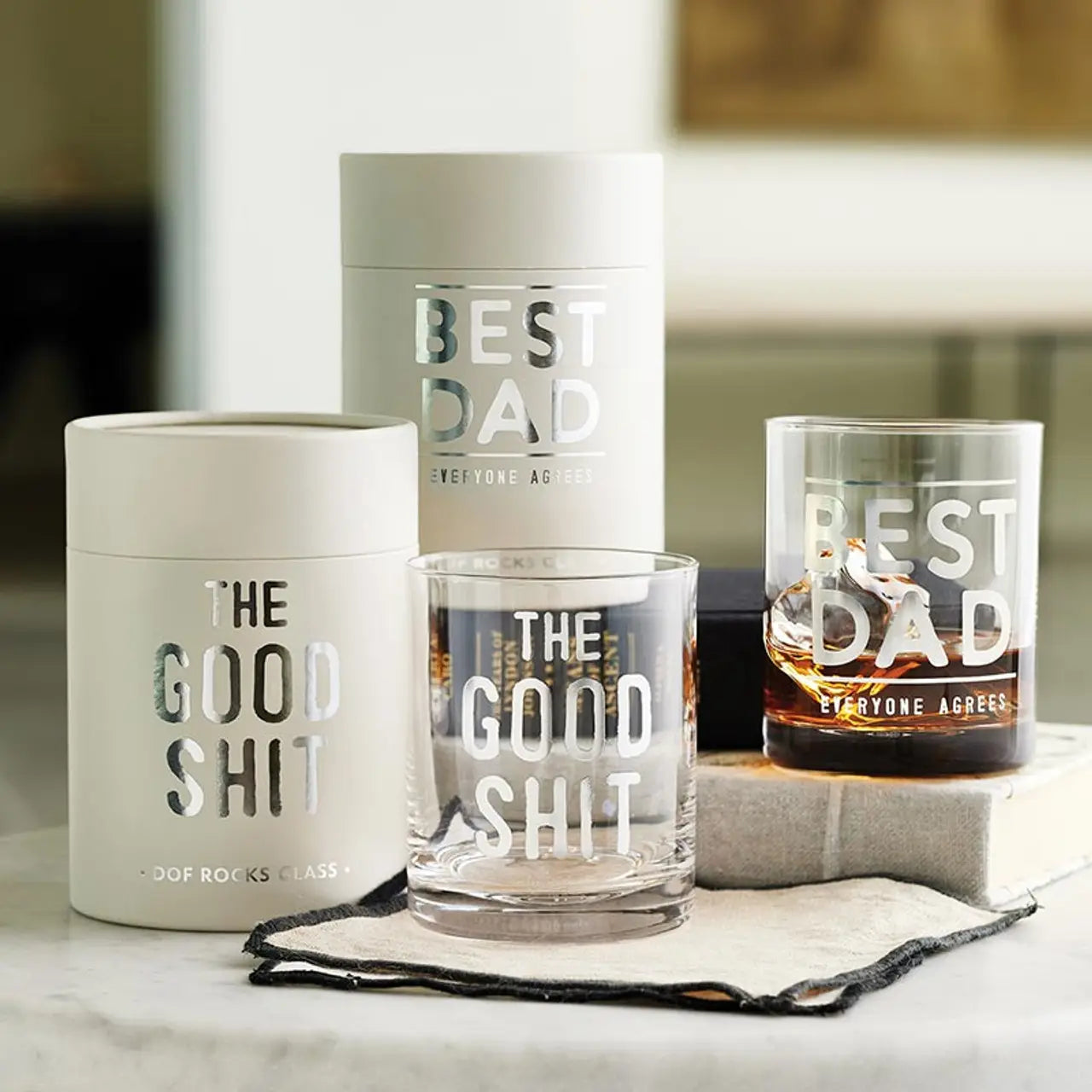 Two glass tumblers with humorous text and a container labeled 'Best Dad' on a surface.