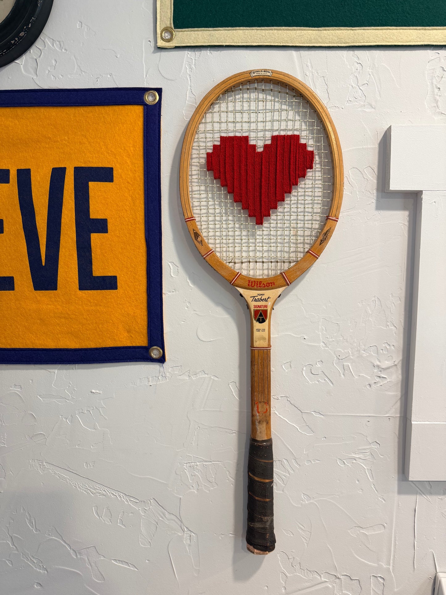 Vintage tennis racket with a red heart design on a textured white wall.