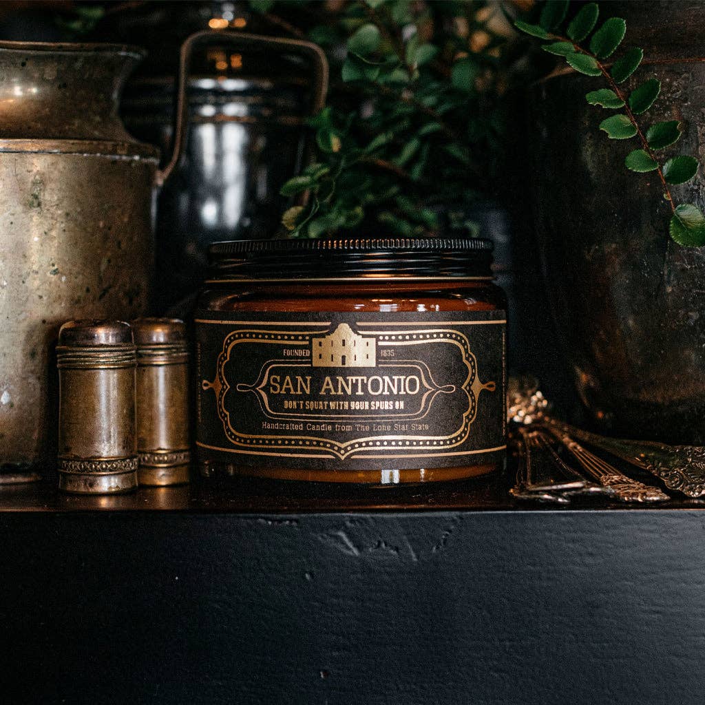 Candle jar labeled 'San Antonio' on a dark surface with decorative items.