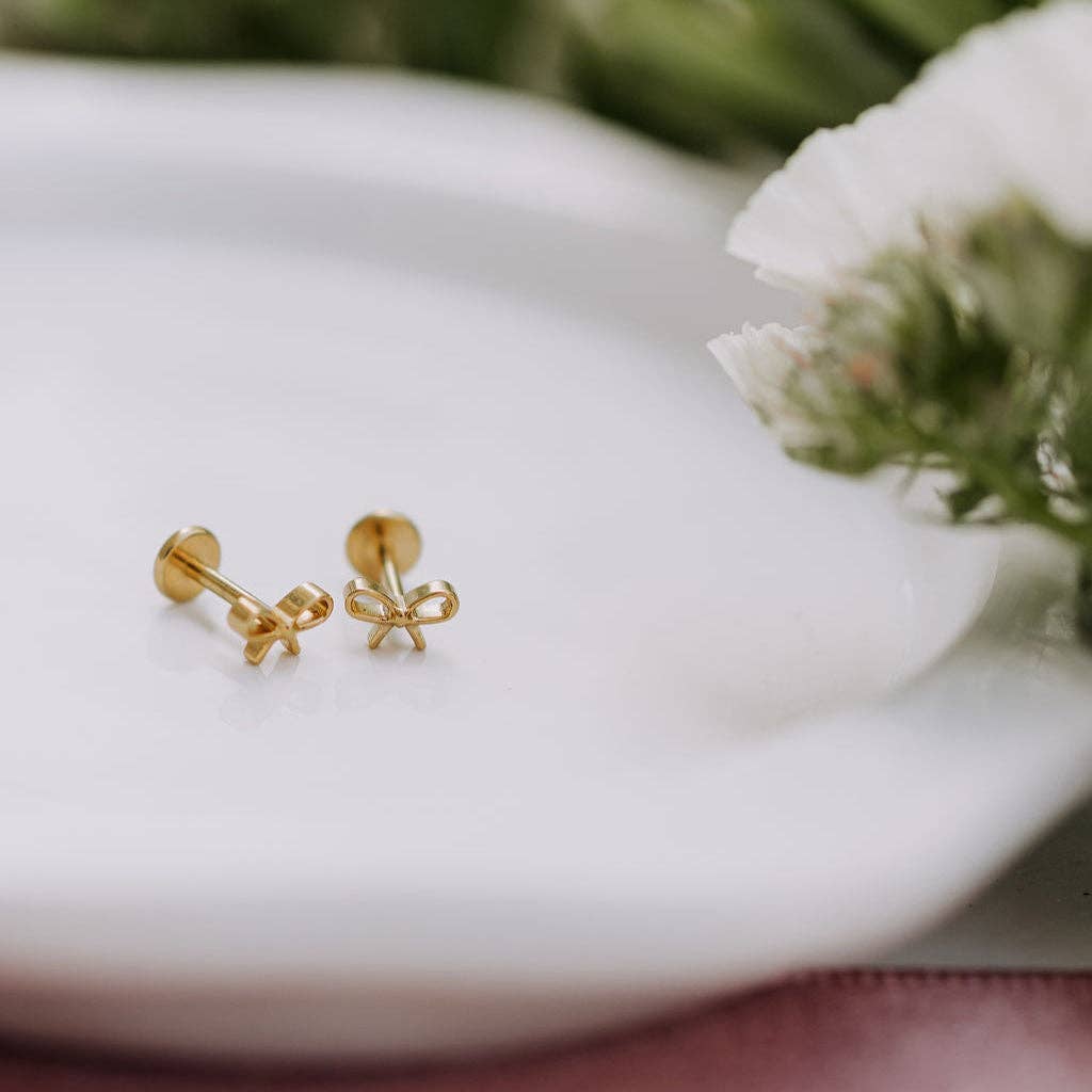 Gold bow-shaped earrings on a white surface with a blurred natural background