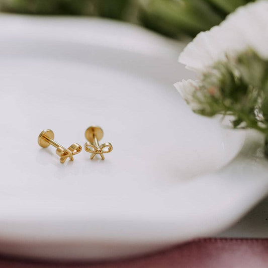 Gold bow-shaped earrings on a white surface with a blurred natural background