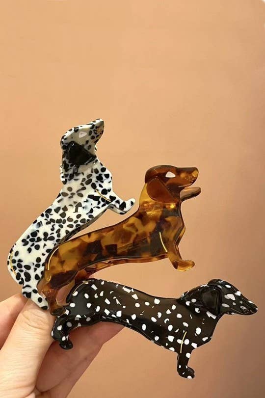 Three dog-shaped hair clips in different styles held against a beige background.
