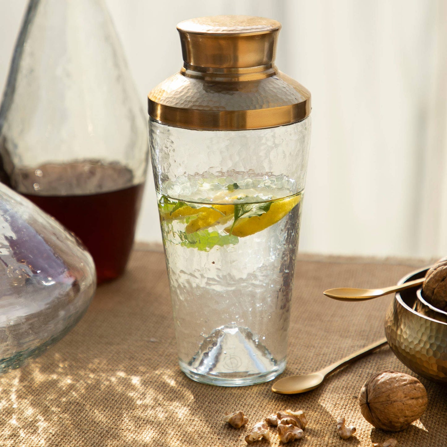 Clear glass carafe with gold lid on a textured surface with a blurred background