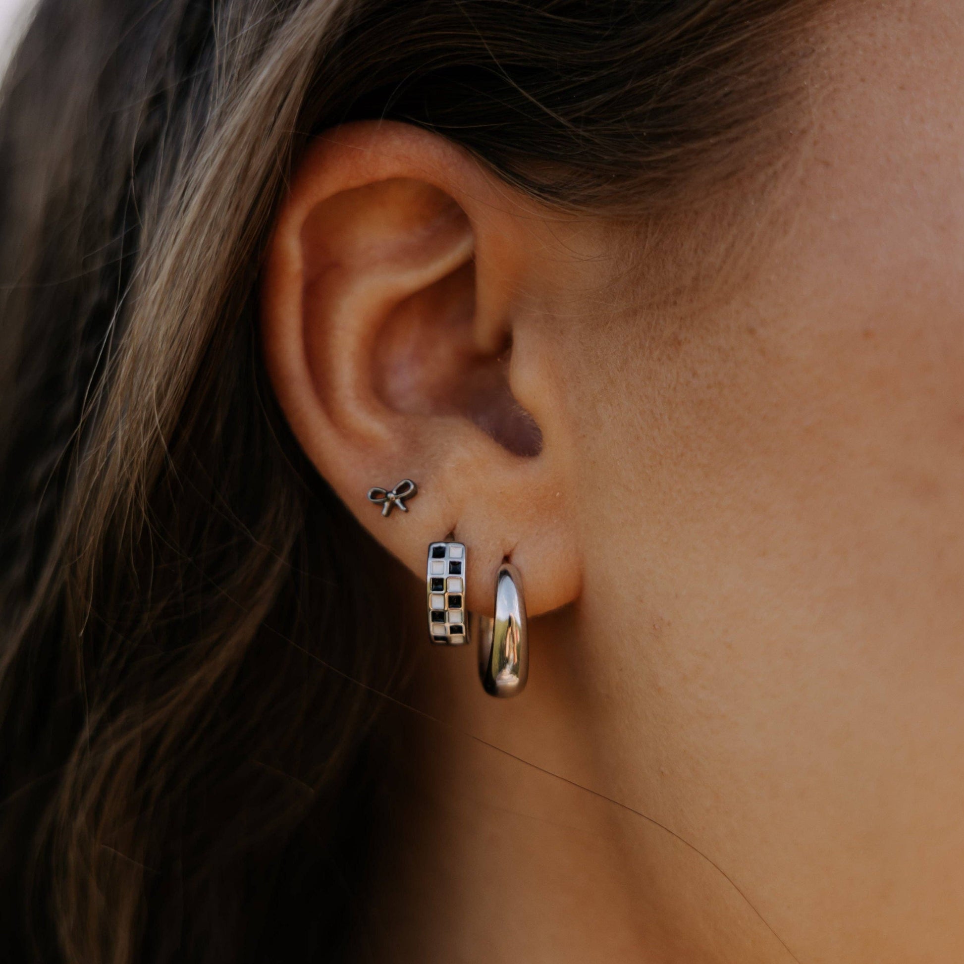 Close-up of an ear wearing three earrings with a neutral background