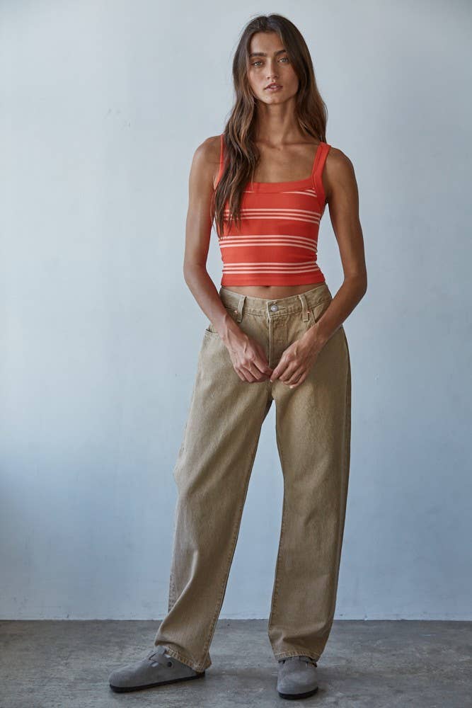 Woman wearing a red striped tank top and beige pants against a plain background