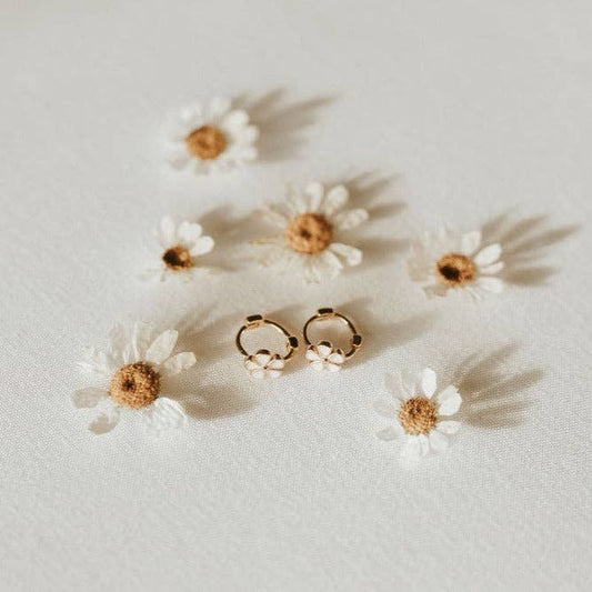 Gold hoop earrings on a light surface with small white flowers.